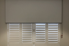 Varas Blockout White in a White Square Faced Top Cassette over a plantation shutter not our shutter